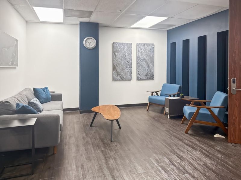A modern office waiting area featuring a blue accent wall, suspended ceiling with recessed lighting, and durable wood-look laminate flooring.