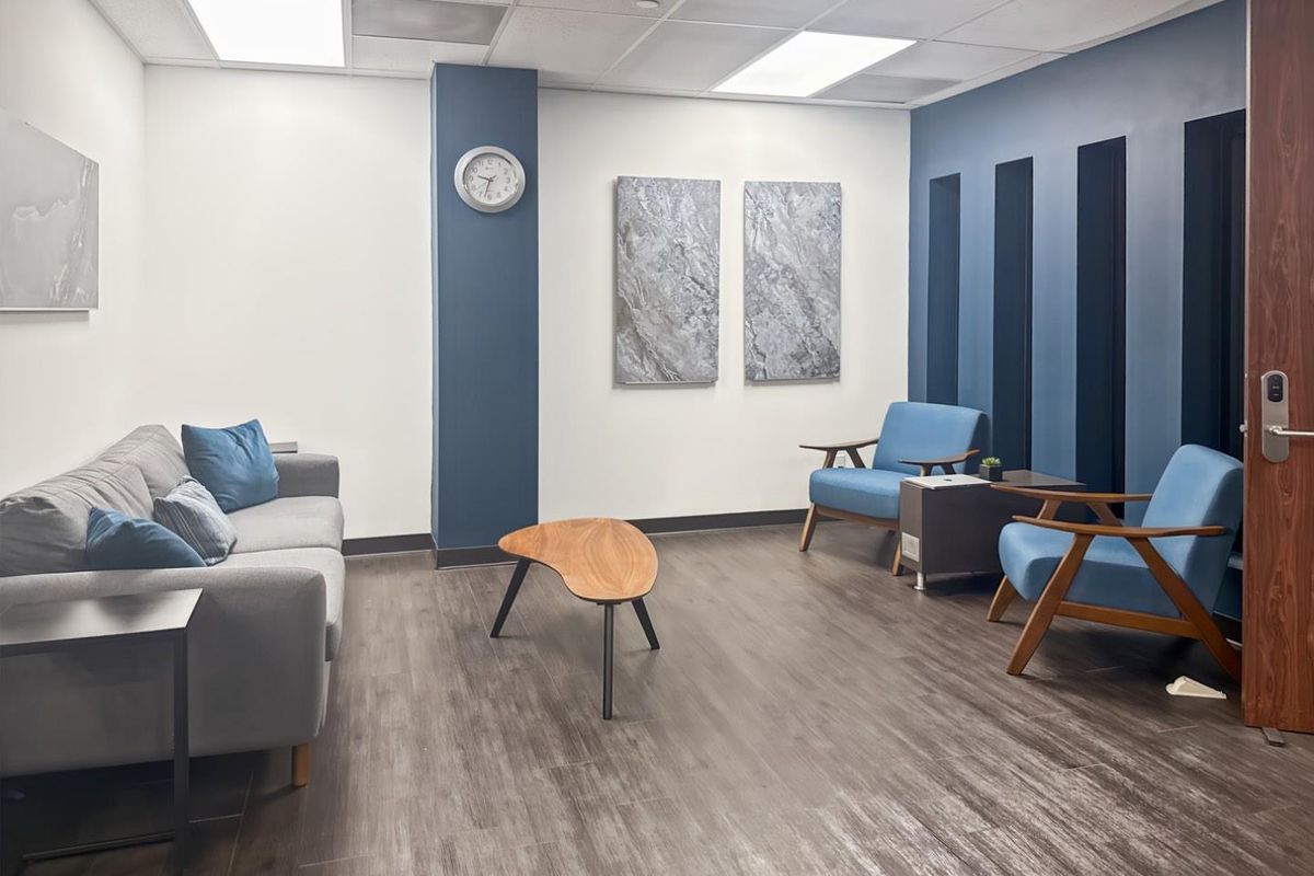 A modern office waiting area featuring a blue accent wall, suspended ceiling with recessed lighting, and durable wood-look laminate flooring.