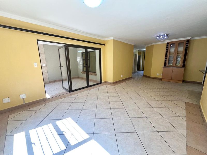 Spacious open-plan living area featuring neutral tiled flooring, built-in cabinetry, and large aluminium sliding doors leading to an enclosed patio space.
