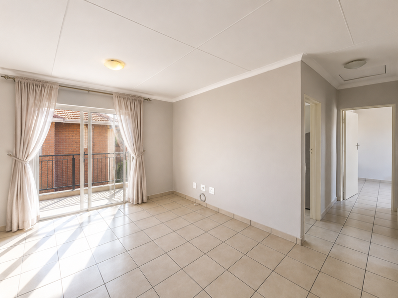 A bright, empty living room featuring neutral tiled flooring, coved ceilings, and a sliding glass door providing access to a balcony.