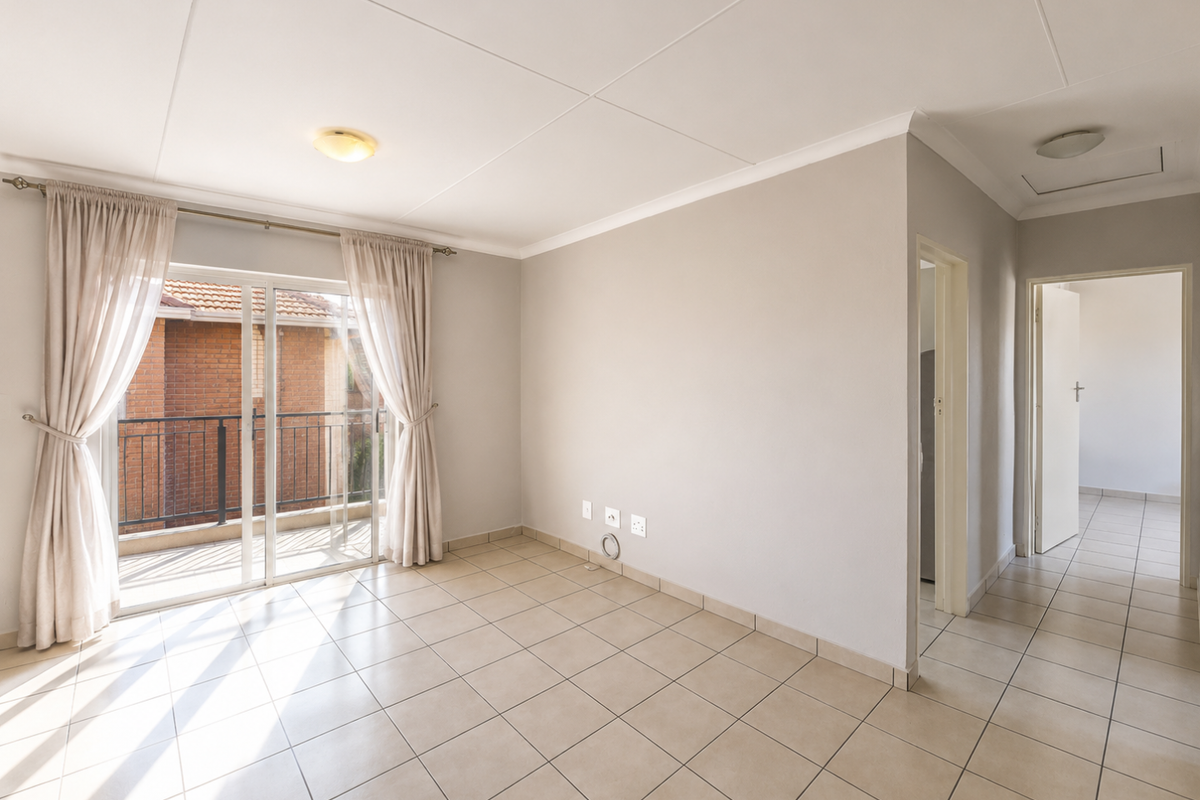 A bright, empty living room featuring neutral tiled flooring, coved ceilings, and a sliding glass door providing access to a balcony.