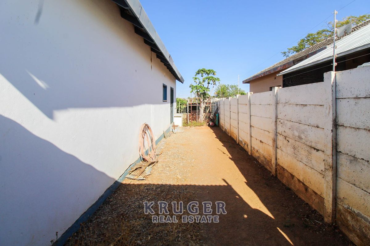 A narrow side yard area featuring a precast concrete boundary wall and gravel ground surface along the side of the house.