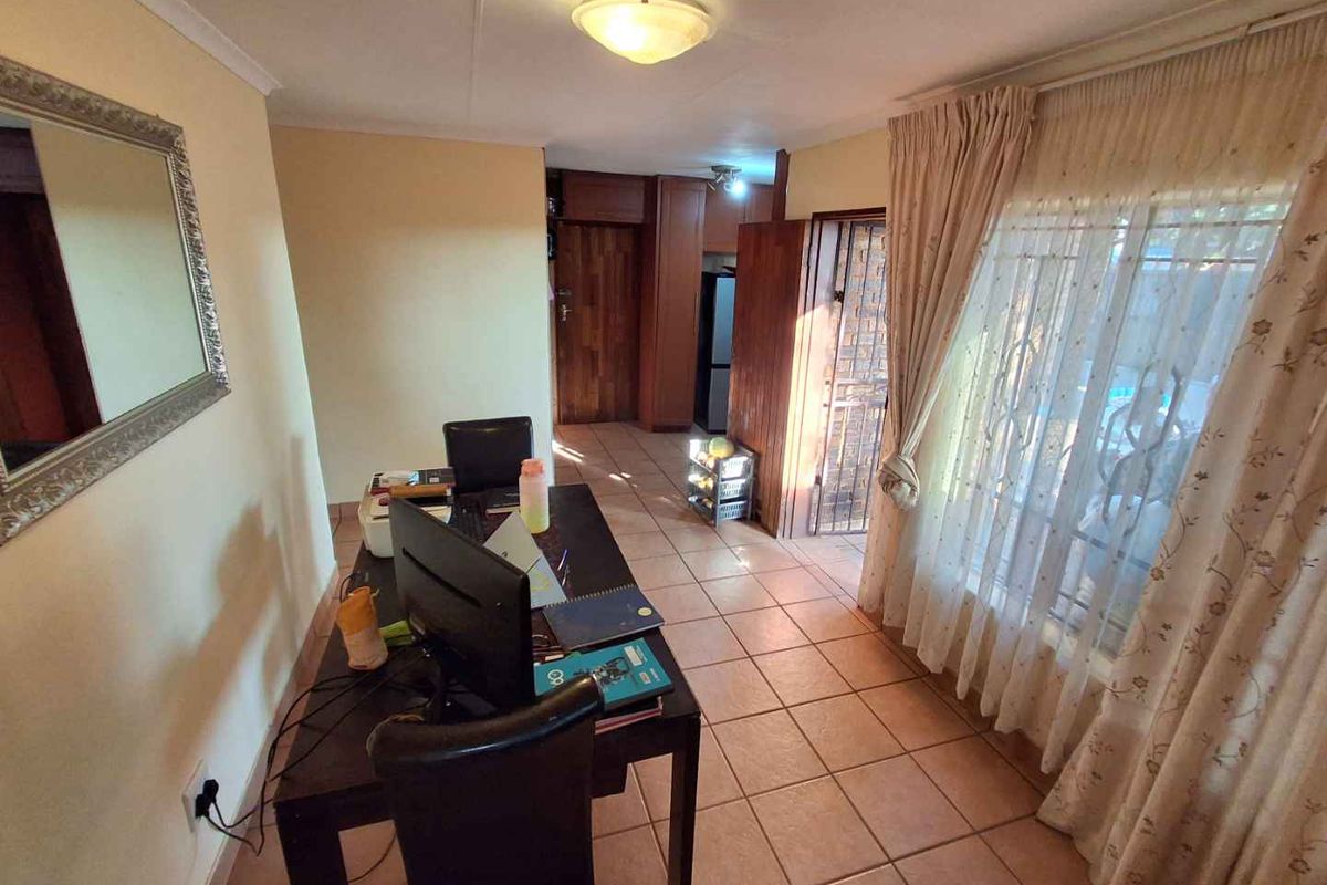 A functional living area featuring tiled flooring, built-in wooden cabinetry, and large windows with natural light, suitable for a home office or lounge space.