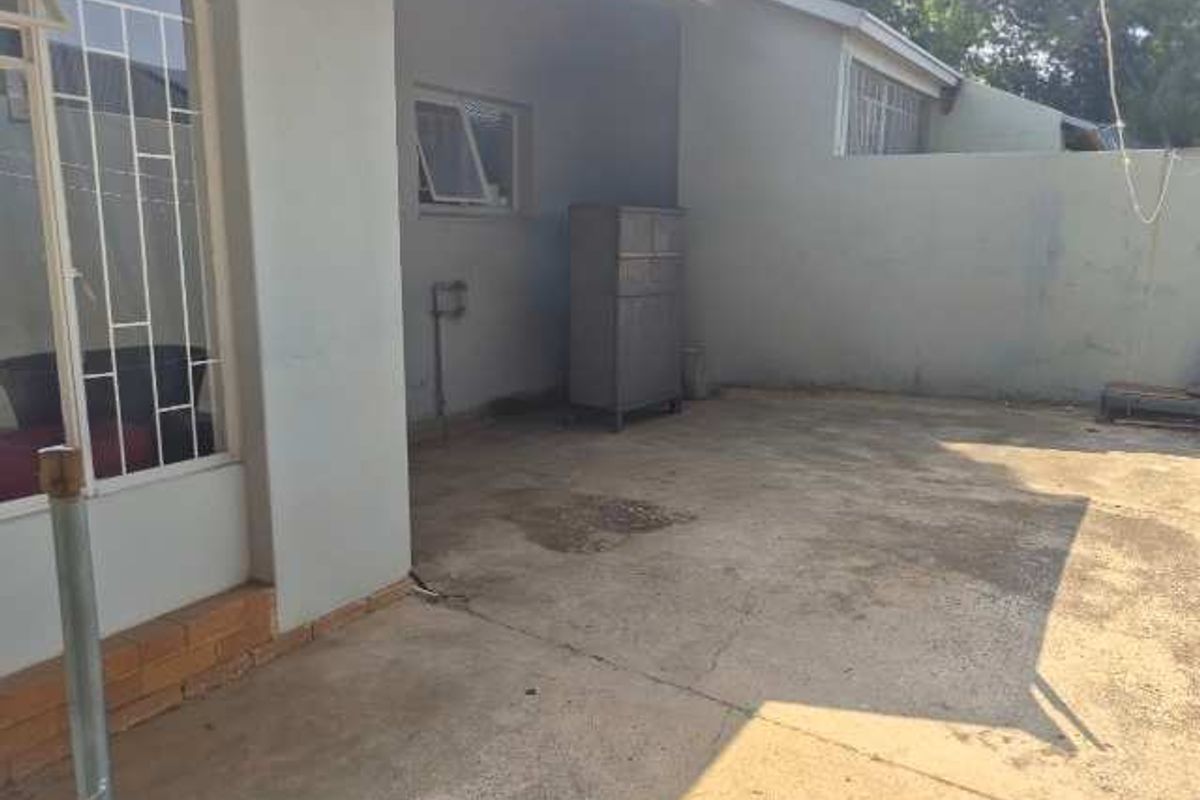 A paved rear courtyard area featuring boundary walls and security-fitted windows, offering a functional outdoor space with potential for landscaping or patio development.