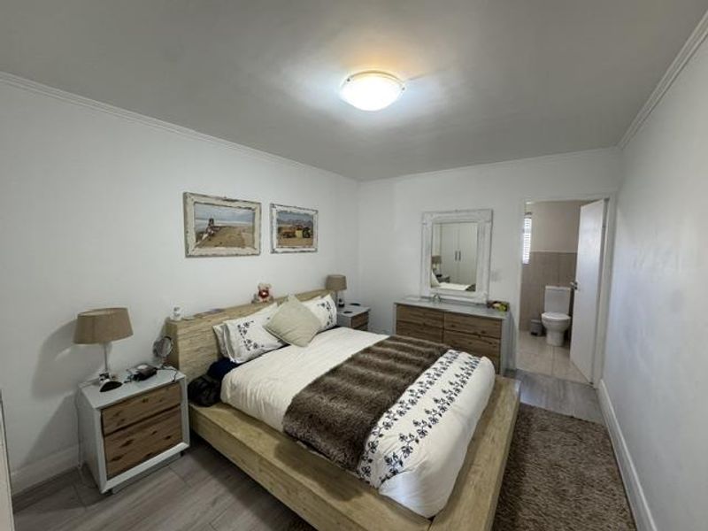 A well-maintained bedroom featuring laminate flooring, neutral walls, and an en-suite bathroom access.