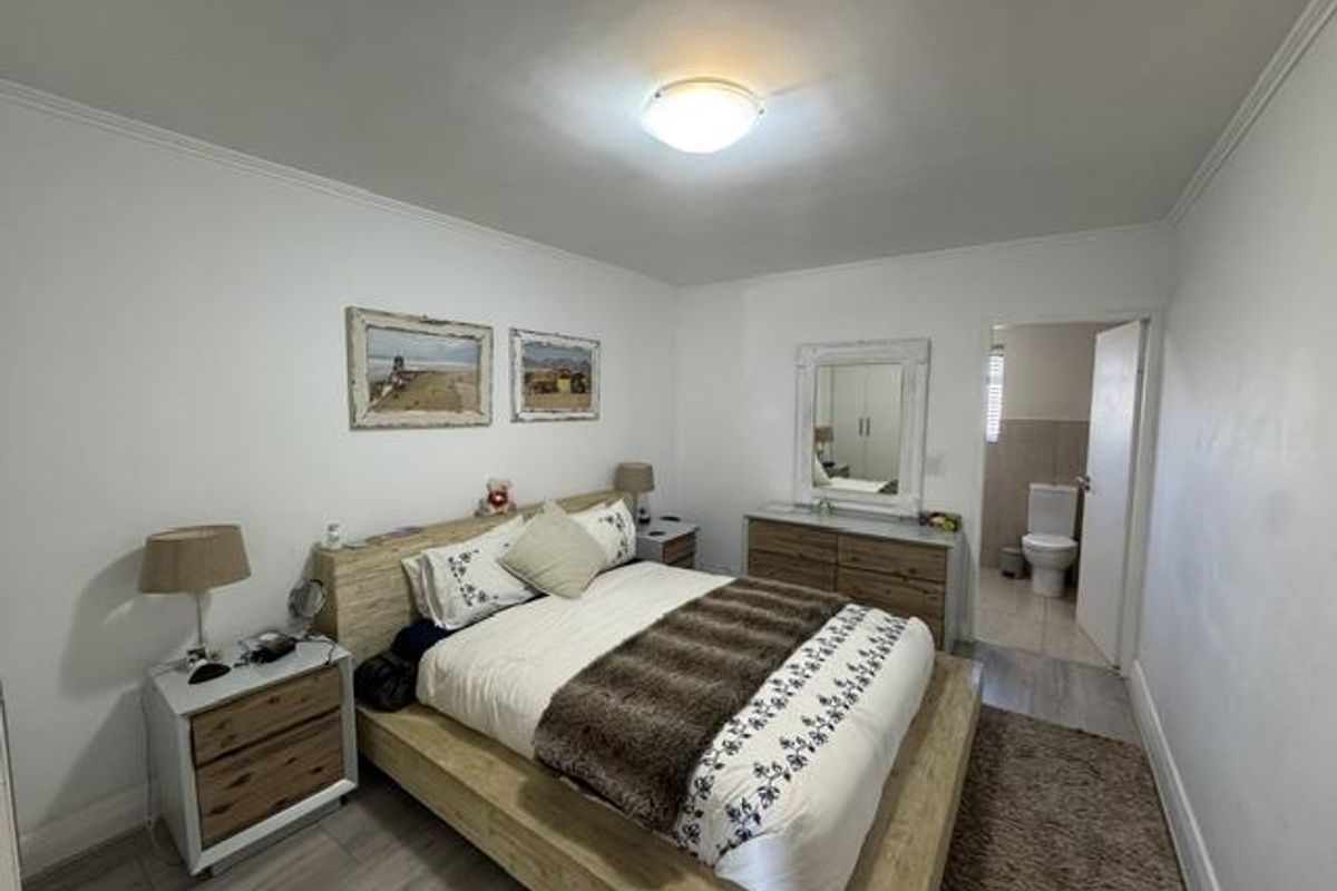 A well-maintained bedroom featuring laminate flooring, neutral walls, and an en-suite bathroom access.