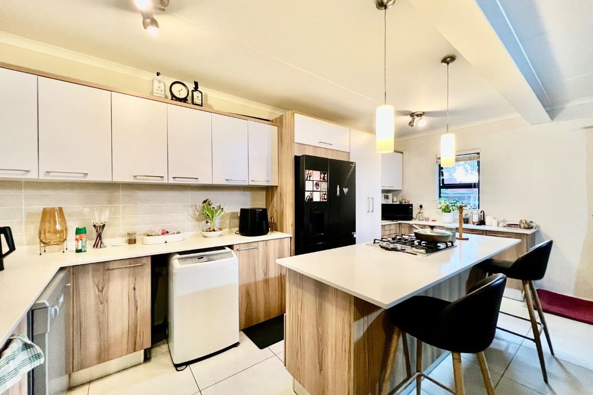 Modern kitchen featuring a central island with gas hob, ample built-in cabinetry, stone countertops, and contemporary pendant lighting.