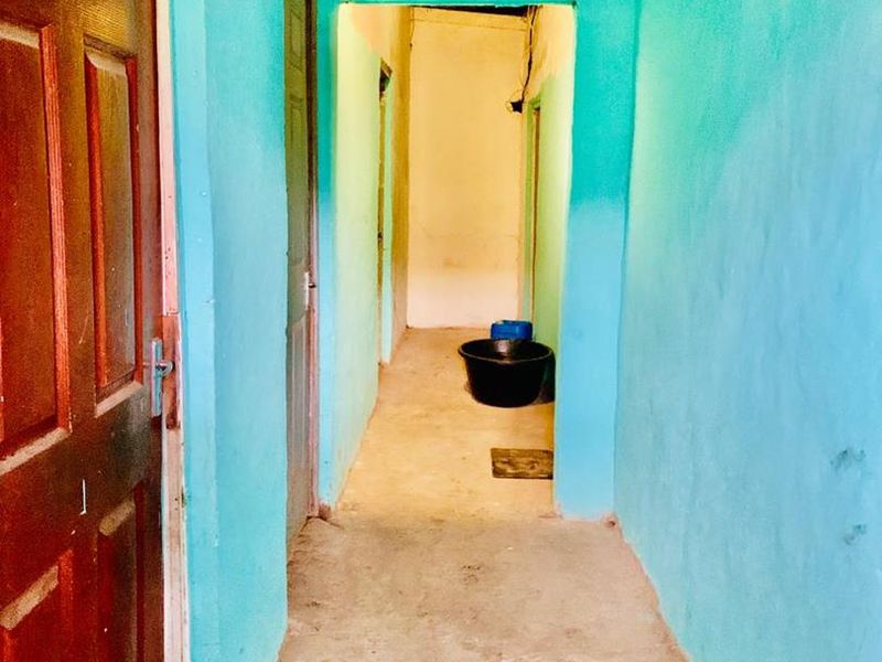 A narrow interior hallway with concrete flooring and brightly painted walls, showing signs of wear and requiring cosmetic updates.