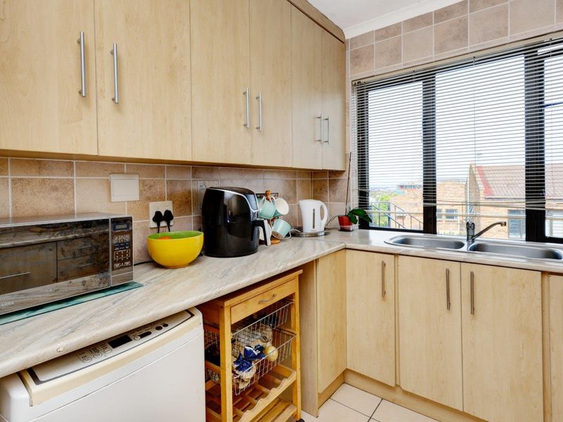 A functional kitchen featuring light wood-finish cabinetry, laminate countertops, a double stainless steel sink, and tiled backsplash with natural light from the window.
