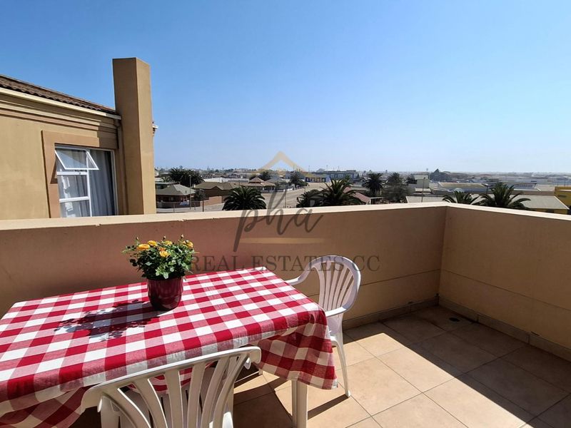 A spacious open-air balcony featuring tiled flooring and a solid masonry balustrade, offering expansive views of the surrounding neighborhood.