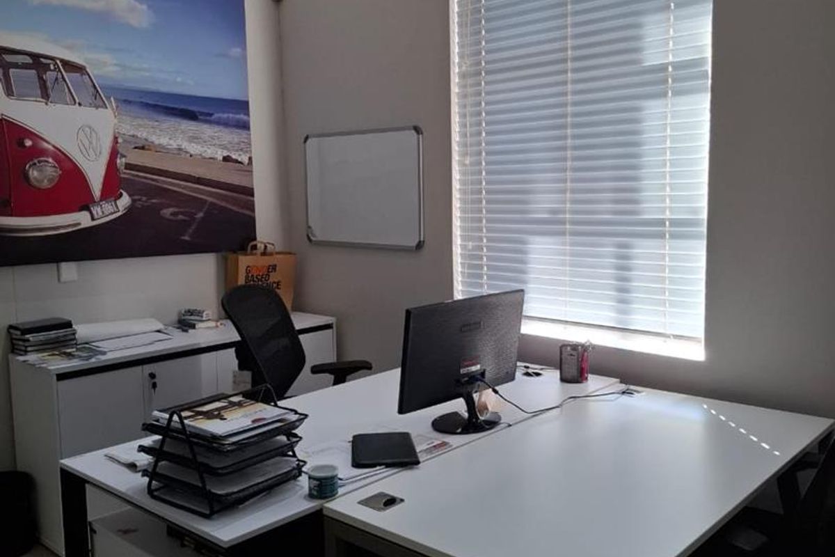 A functional office space featuring tiled flooring, a wall-mounted split-system air conditioner, and venetian blinds for light control.