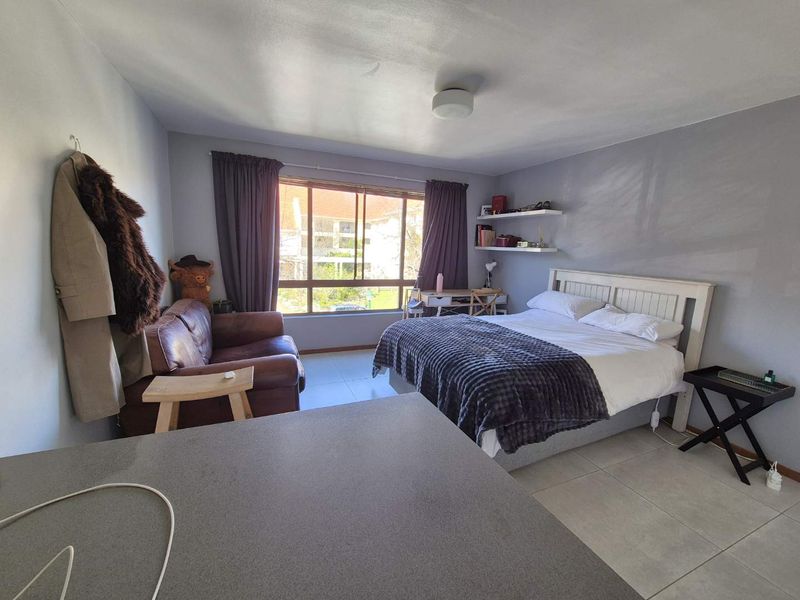 A bedroom featuring tiled flooring, a large window providing natural light, and floating wall shelves.