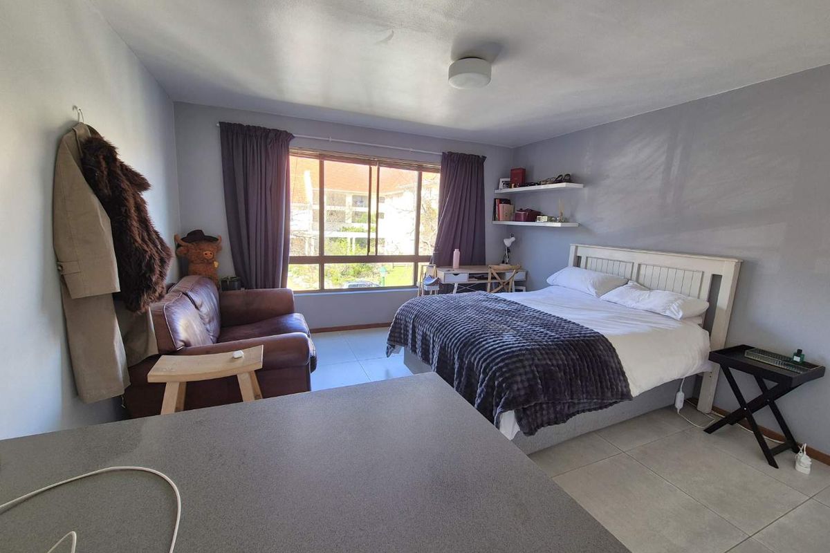 A bedroom featuring tiled flooring, a large window providing natural light, and floating wall shelves.