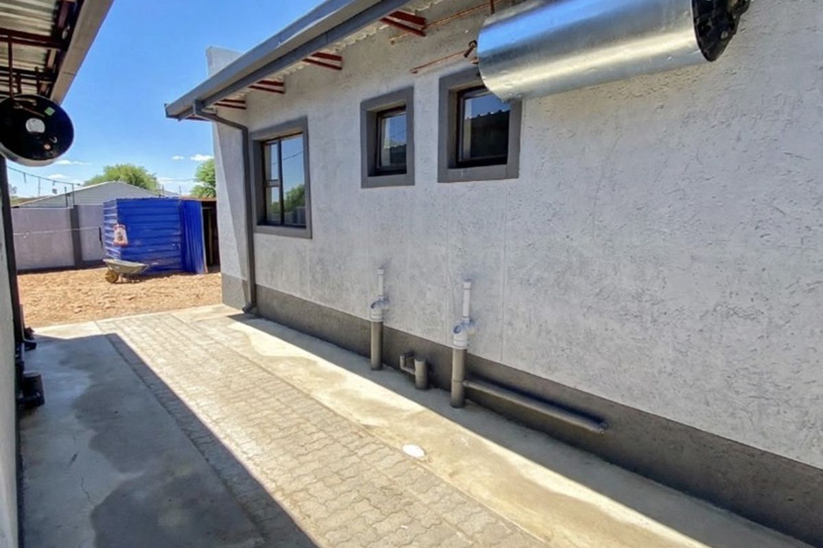 Rear exterior view of the property featuring a paved walkway, external geyser installation, and exposed plumbing connections along the side wall.
