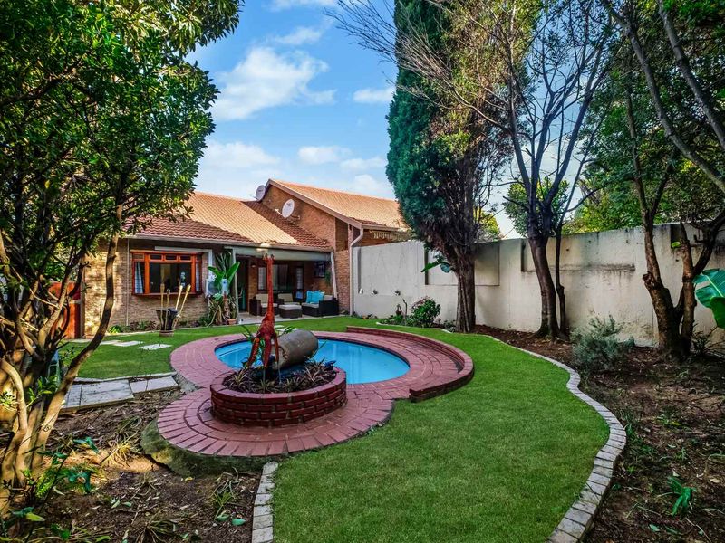 Rear garden featuring a swimming pool with brick surround, established trees, and a tiled roof house facade.
