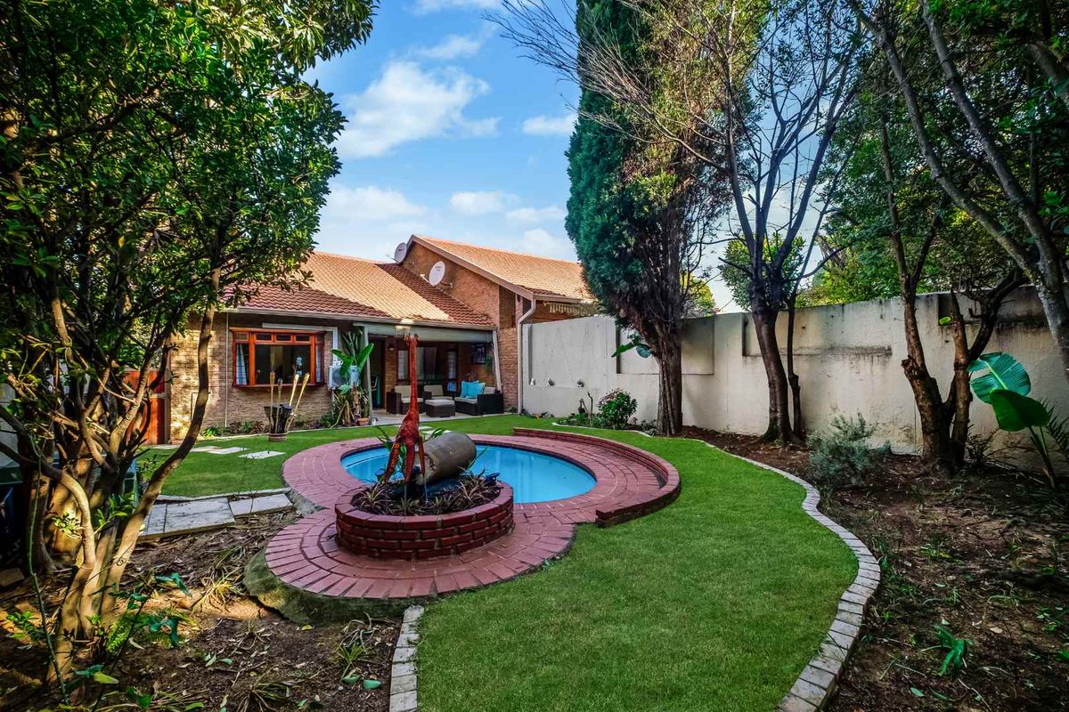 Rear garden featuring a swimming pool with brick surround, established trees, and a tiled roof house facade.