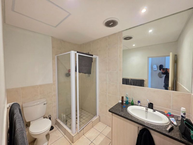 A functional bathroom featuring a shower enclosure, vanity cabinet with integrated sink, toilet, and large wall mirror with neutral tiled finishes.