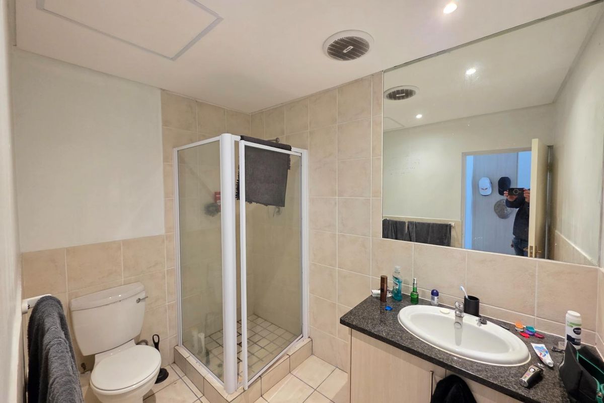 A functional bathroom featuring a shower enclosure, vanity cabinet with integrated sink, toilet, and large wall mirror with neutral tiled finishes.