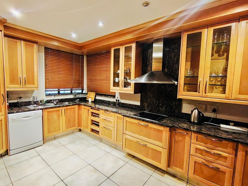 A well-maintained kitchen featuring wooden cabinetry, granite countertops, a stainless steel extractor fan, and tiled flooring with recessed lighting.