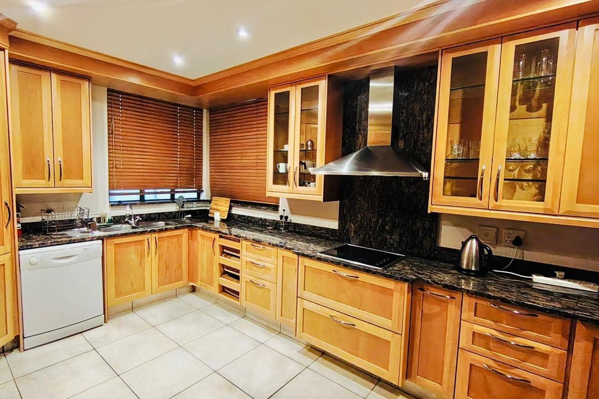 A well-maintained kitchen featuring wooden cabinetry, granite countertops, a stainless steel extractor fan, and tiled flooring with recessed lighting.