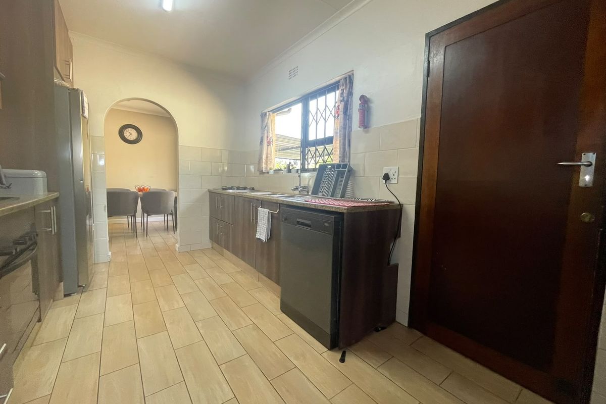 A functional kitchen featuring tiled flooring, built-in cabinetry, and a tiled backsplash, with an open archway leading to the adjacent dining area.