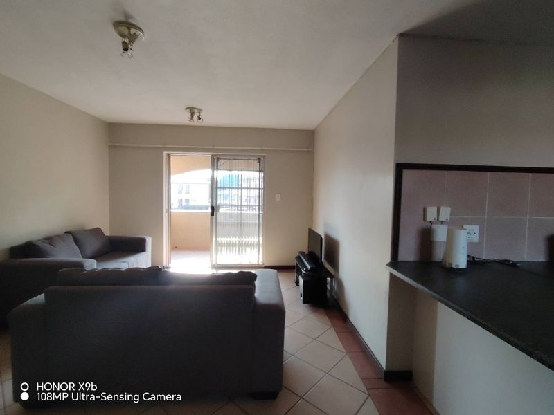 Open plan living area featuring tiled flooring, a kitchen counter with splashback, and a sliding door leading to a balcony.