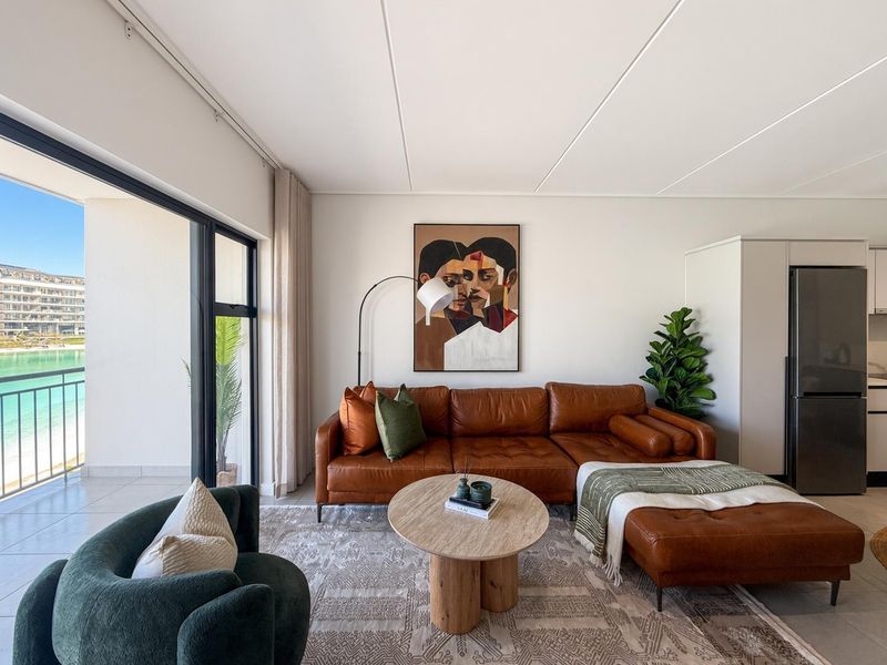 Modern open-plan living area featuring tiled floors, sleek built-in cabinetry, and a large sliding glass door opening onto a balcony with water views.