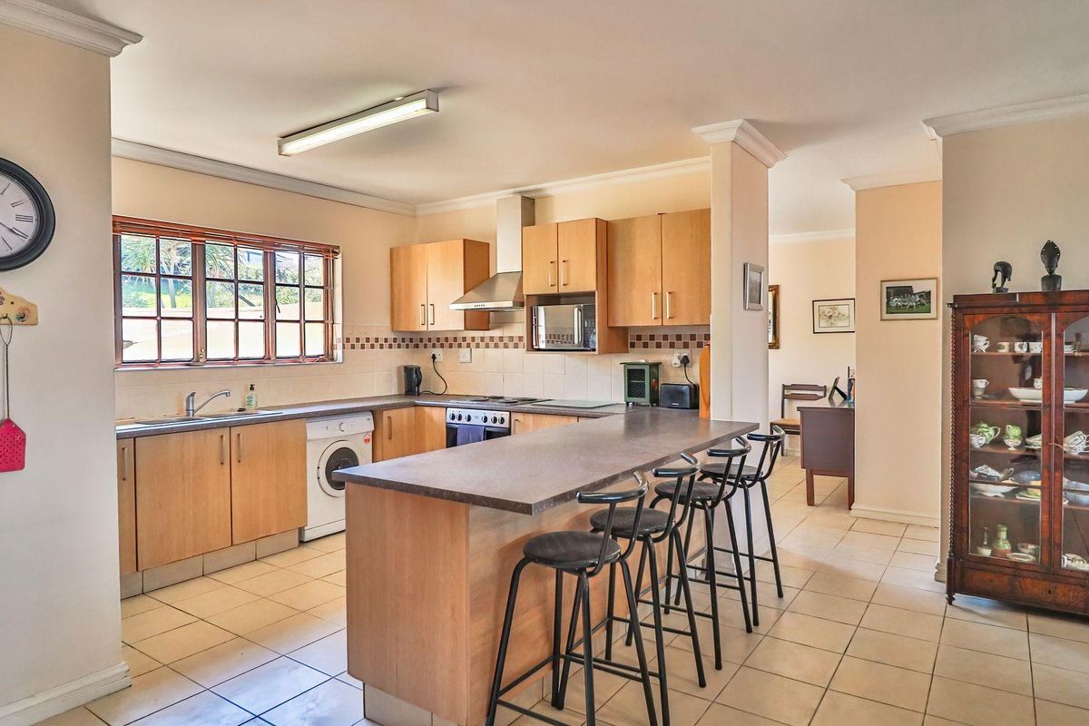 A functional kitchen featuring light wood cabinetry, laminate countertops, a breakfast bar, and tiled flooring, with an integrated oven and extractor fan.