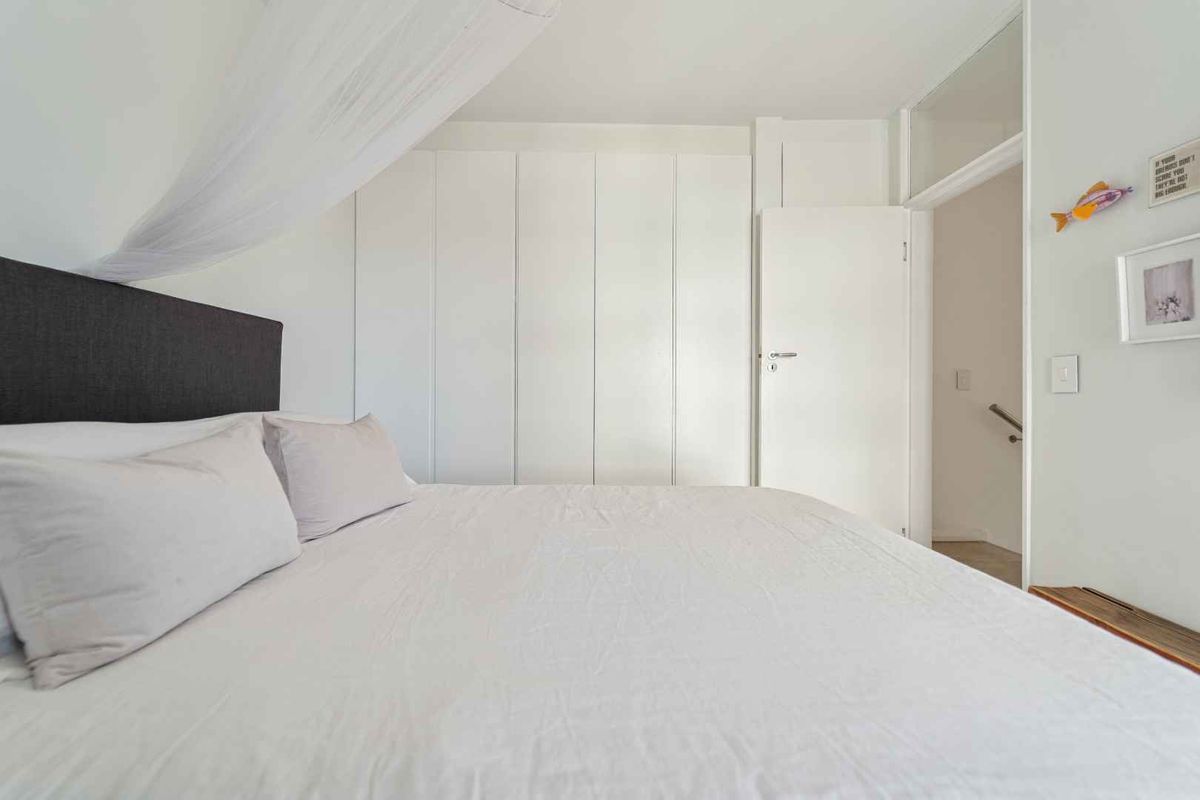 A bright bedroom featuring floor-to-ceiling built-in cupboards and a clean, neutral aesthetic with a transom window above the doorway.