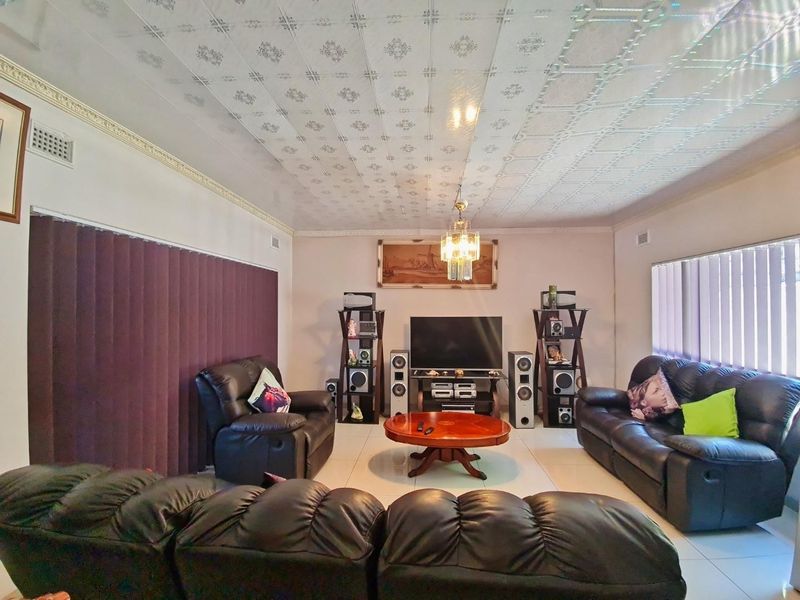 A spacious living room featuring tiled flooring, decorative ceiling tiles, crown molding, and vertical blinds, offering a functional and comfortable living space.