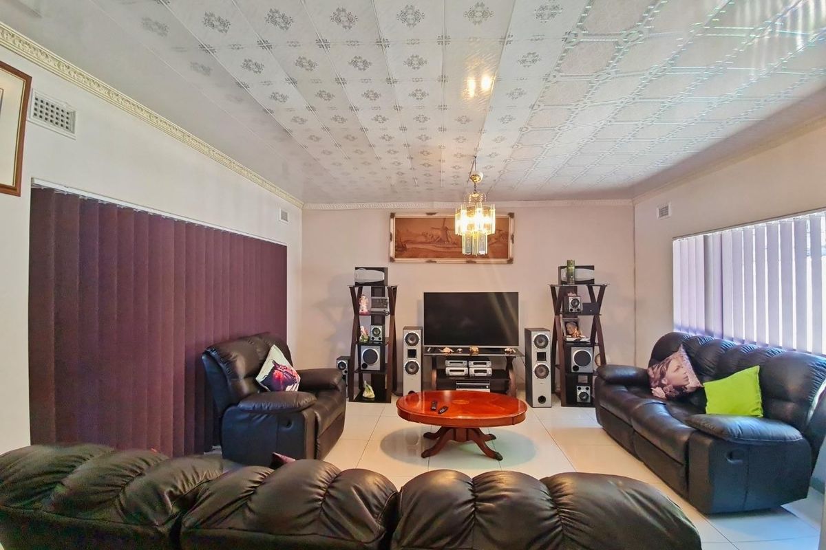 A spacious living room featuring tiled flooring, decorative ceiling tiles, crown molding, and vertical blinds, offering a functional and comfortable living space.
