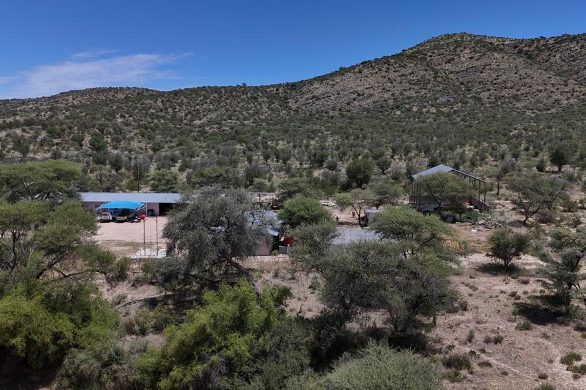 Aerial view of a rural farm property featuring multiple outbuildings, a carport, and expansive natural landscape set against a mountain backdrop.