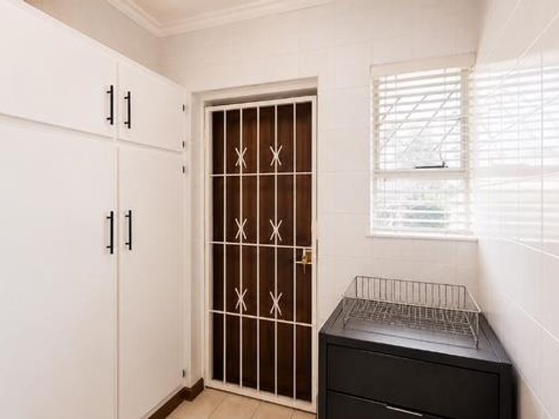 A functional scullery or utility area featuring built-in white cabinetry, tiled walls, and a secure exterior door with a metal security gate.