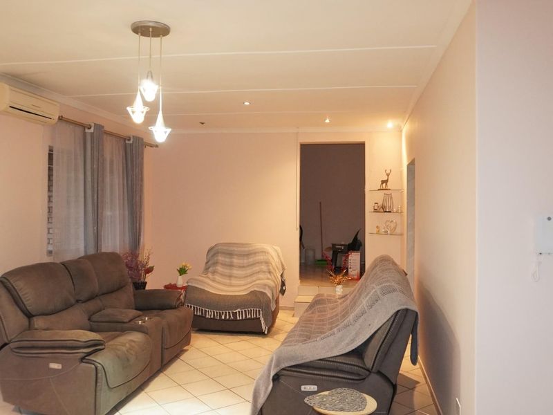A living room featuring tiled flooring, recessed downlights, and a wall-mounted air conditioning unit, with access to an outdoor area through a security gate.