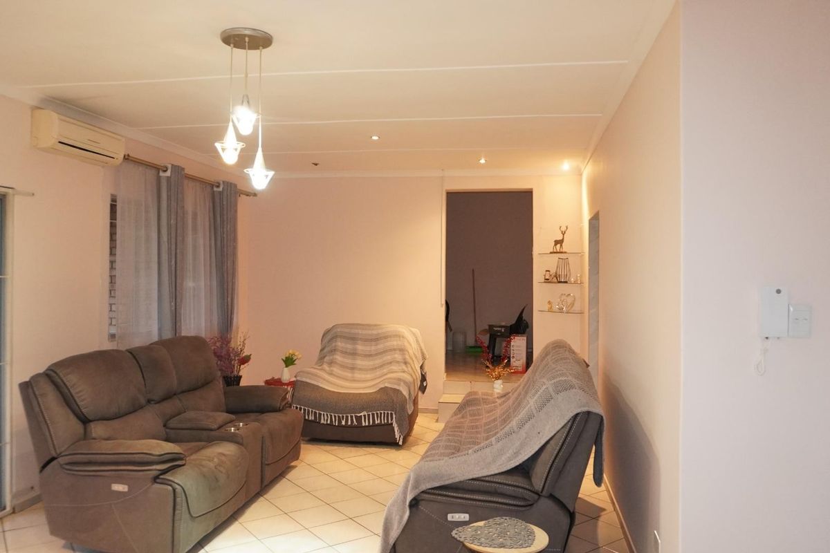 A living room featuring tiled flooring, recessed downlights, and a wall-mounted air conditioning unit, with access to an outdoor area through a security gate.