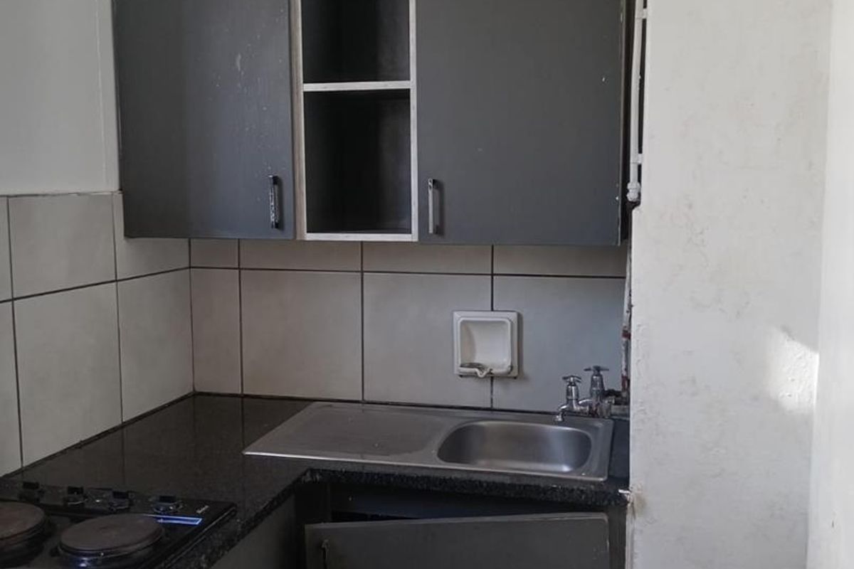 Compact kitchen featuring dark cabinetry, granite countertops, a stainless steel sink, and a built-in hob, requiring cosmetic updates and repairs.