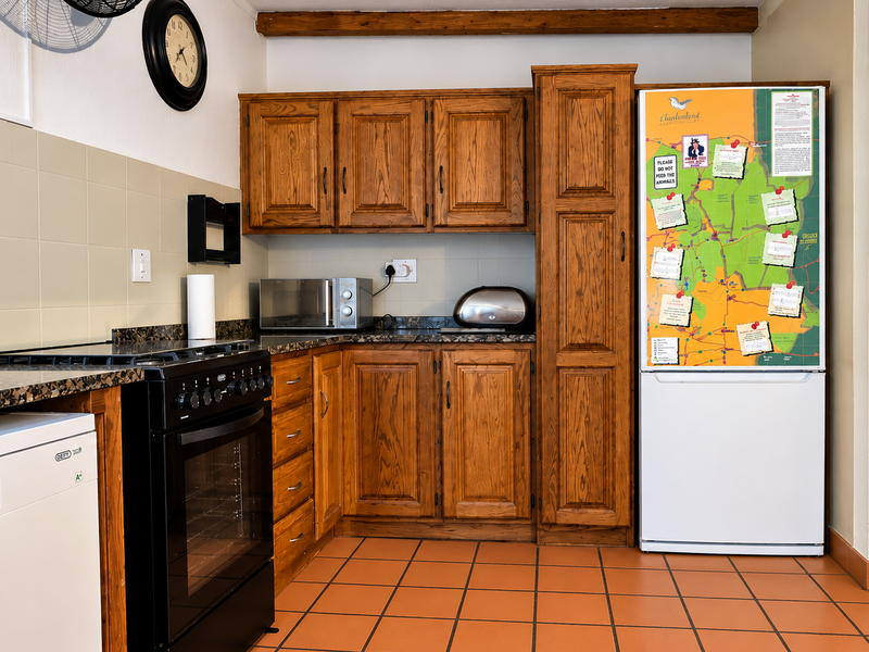A functional kitchen featuring traditional wooden cabinetry, granite countertops, tiled flooring, and a freestanding oven, complemented by an exposed timber ceiling beam.