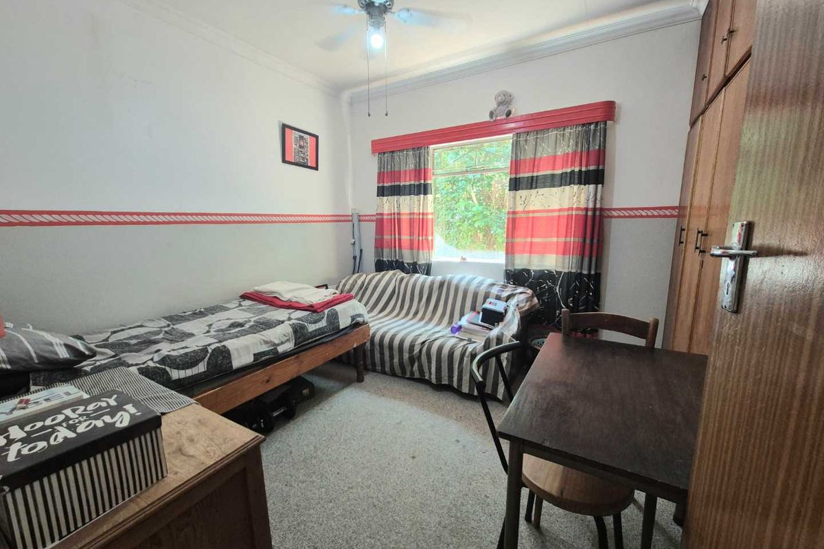 A functional bedroom featuring built-in wooden cabinetry, a ceiling fan, and a window providing natural light.