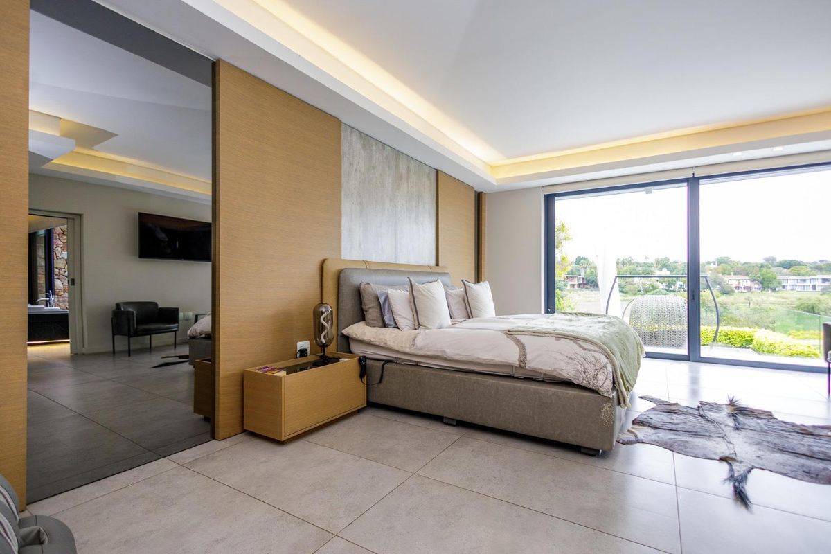 Modern bedroom featuring recessed ceiling lighting, large sliding glass doors leading to a balcony, and a sleek wood-paneled feature wall.