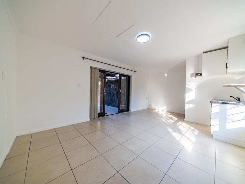 An open-plan living and kitchen area featuring tiled flooring, neutral walls, and a sliding glass door leading to an outdoor space.
