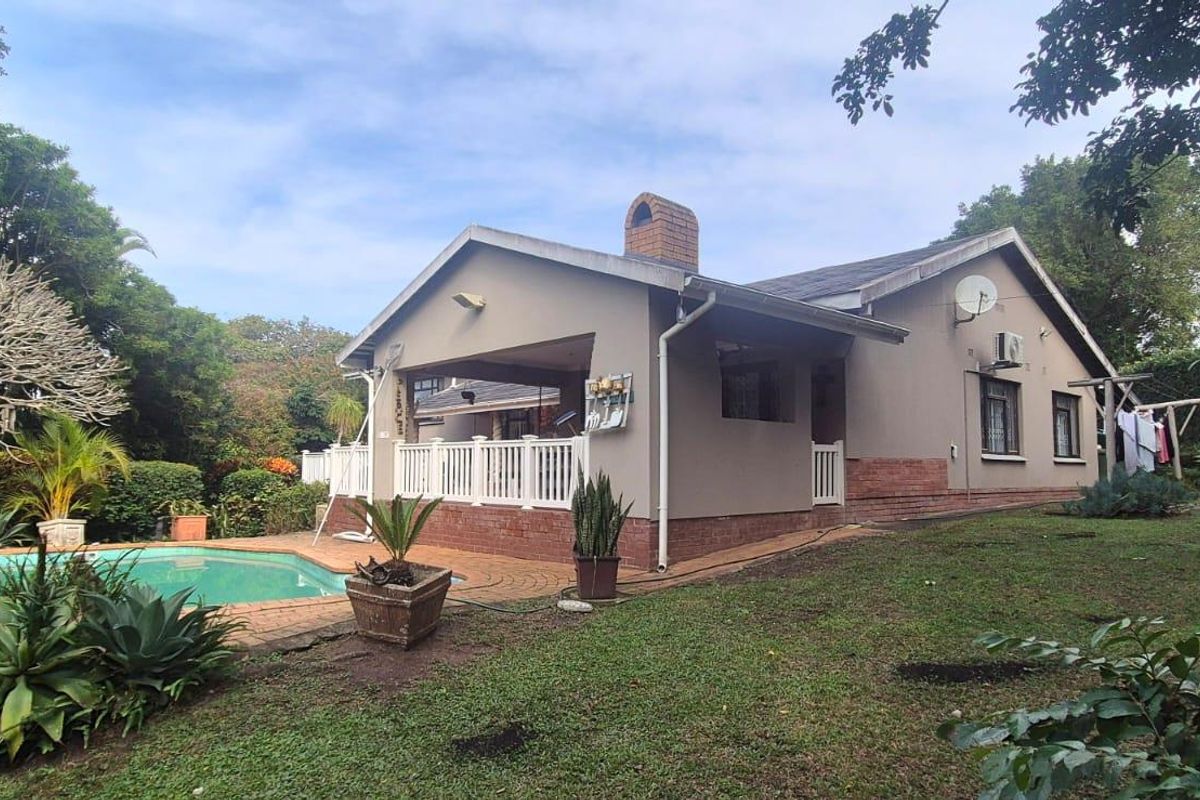 Rear view of the house featuring a covered patio, brick chimney, and a swimming pool set within a landscaped garden.