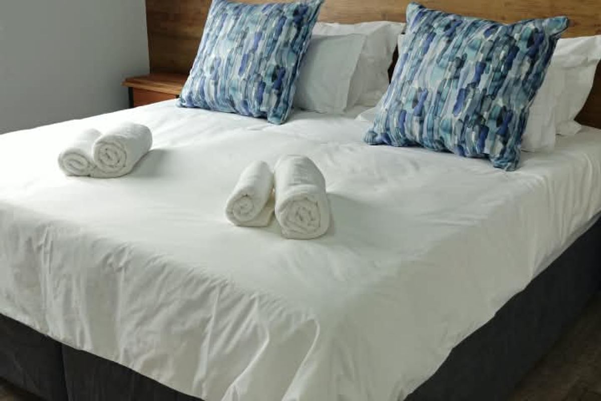 A well-maintained bedroom featuring wood-look laminate flooring and a modern built-in headboard with integrated wall-mounted lighting.