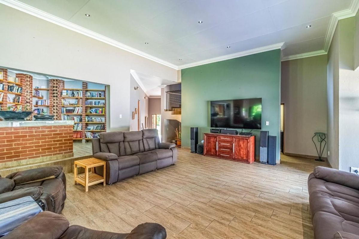 Spacious living room featuring wood-look tile flooring, a striking green accent wall, and a built-in brick bar area with integrated shelving.