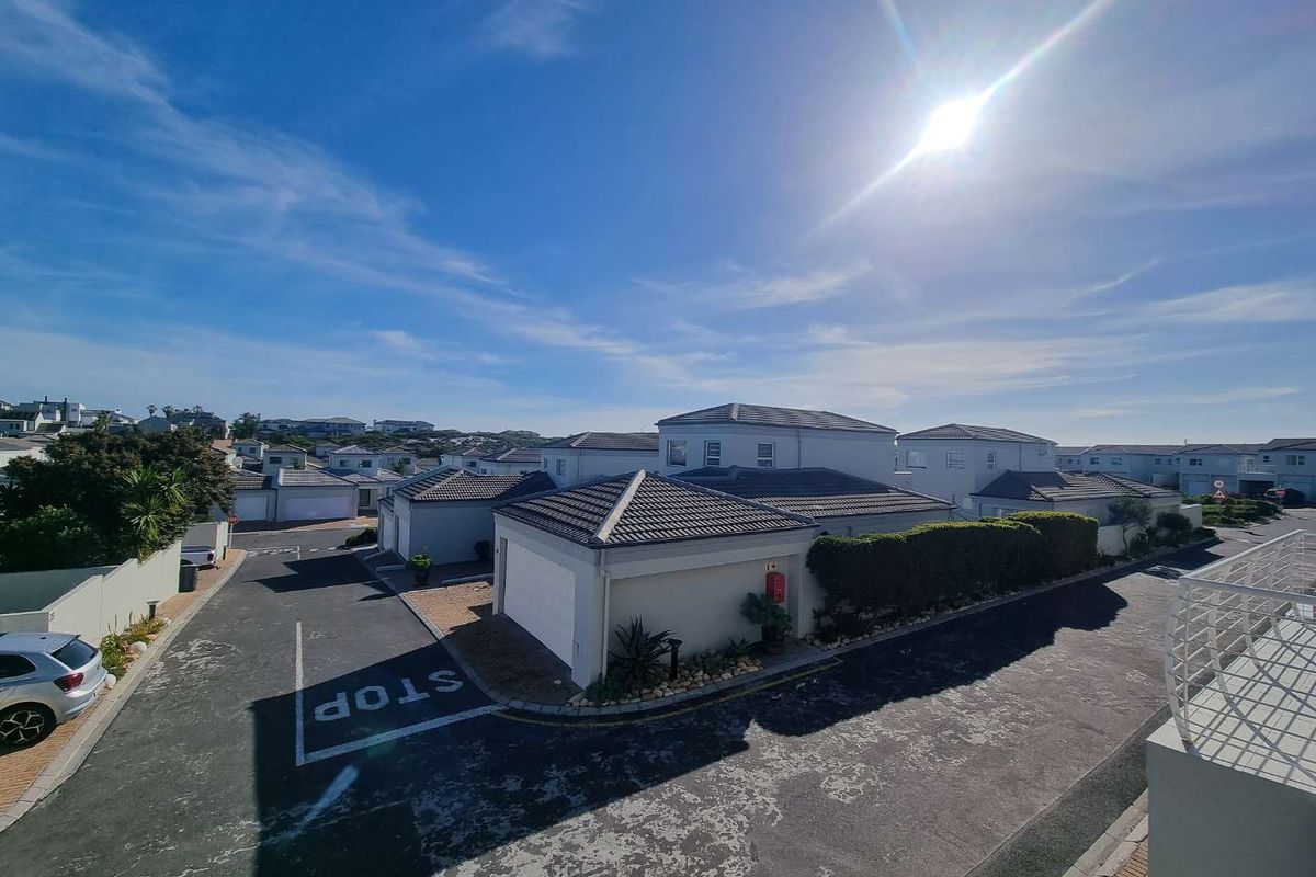 An elevated aerial view of a townhouse complex featuring multiple units with tiled roofs, paved driveways, and established boundary walls.