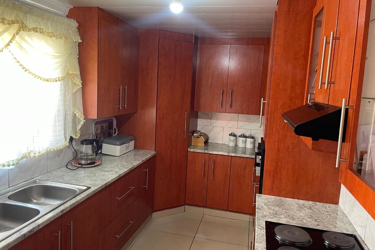 A functional kitchen featuring wood-look cabinetry, laminate countertops, a double stainless steel sink, and built-in cooking appliances with tiled flooring.