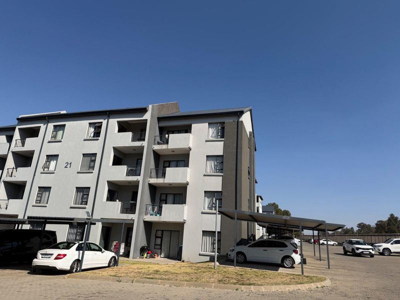 Exterior view of a modern apartment complex featuring multi-level balconies, paved parking areas with covered bays, and well-maintained building facades.