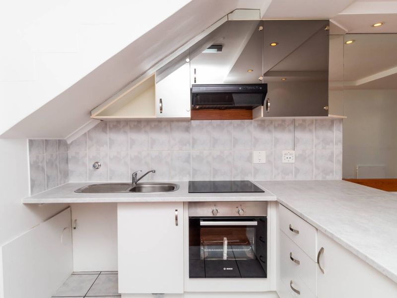 Compact kitchen featuring built-in oven, electric hob, extractor fan, stainless steel sink, and ample cabinetry with neutral tiled backsplash.