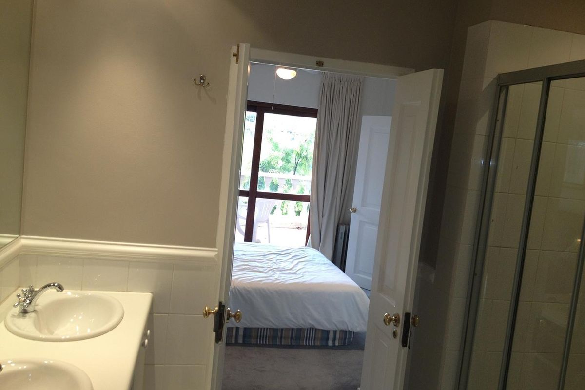 A bathroom featuring a double vanity with white countertops, leading into a bedroom with access to a balcony.