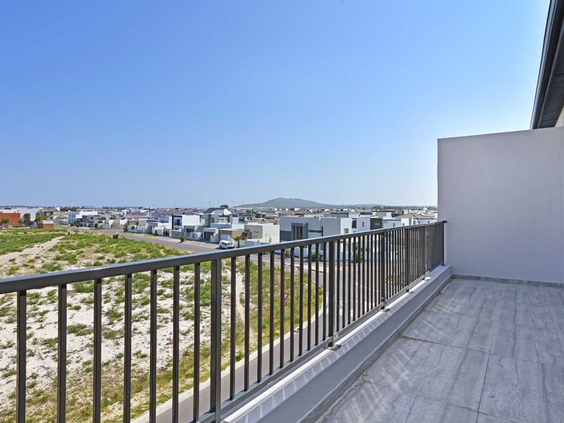 A clean, modern balcony featuring tiled flooring and a metal balustrade, offering an elevated view of the surrounding neighborhood.