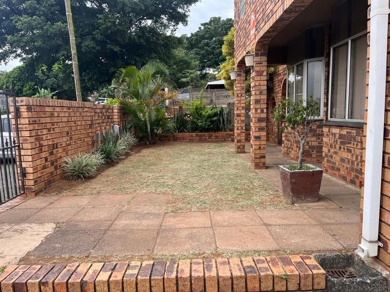 A rear exterior view featuring a face brick facade, covered patio area, and a paved courtyard with a brick boundary wall.